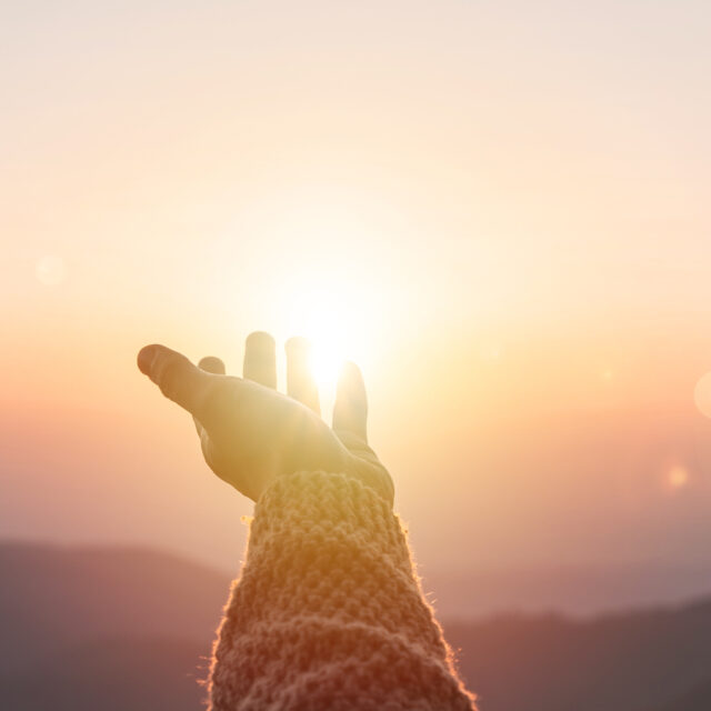Young woman hand reaching for the mountains during sunset and beautiful landscape